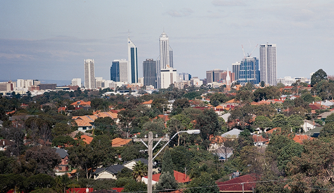 Foreground of house roofs and trees and a background of the city skyline.