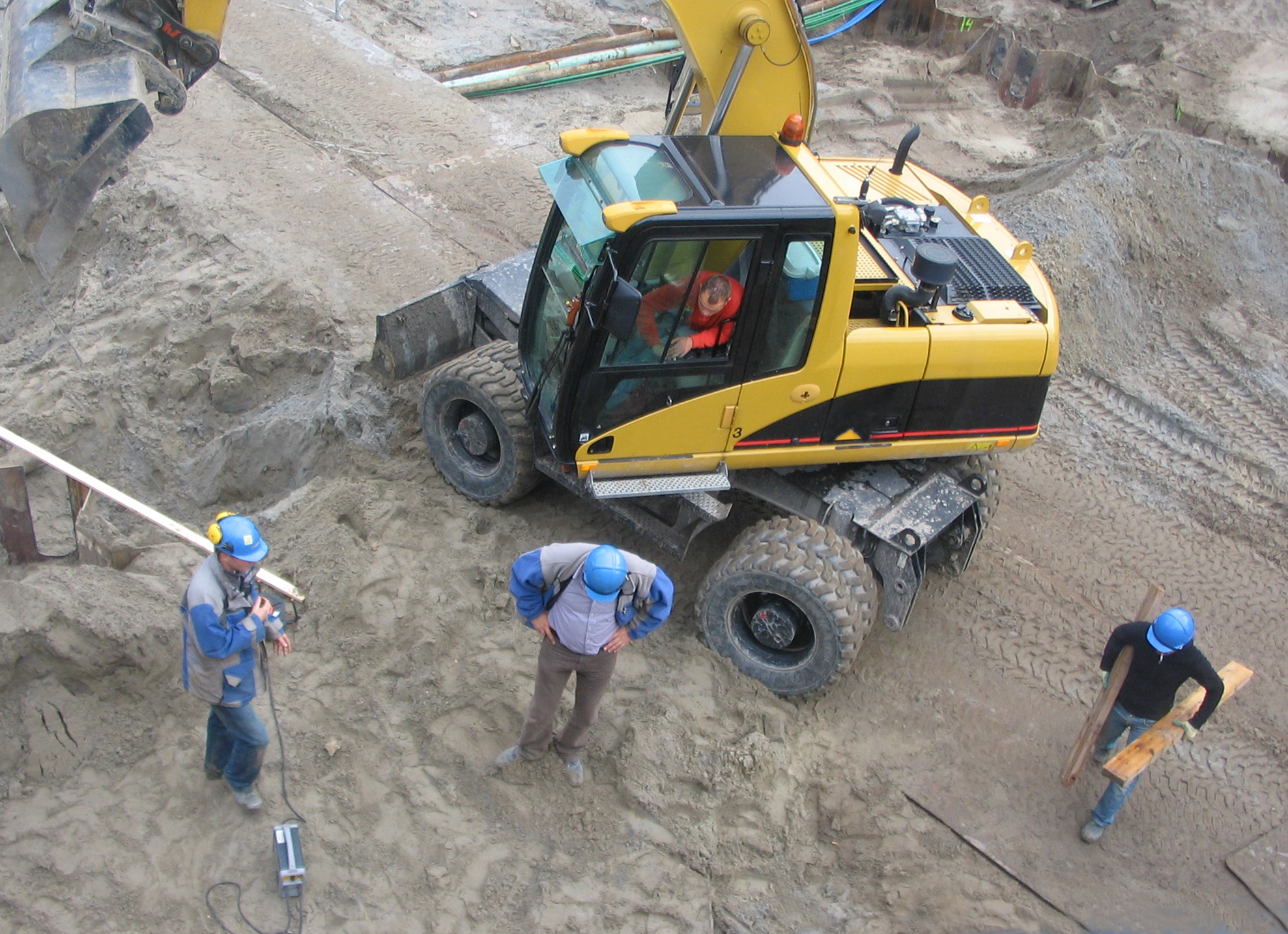 Crane on construction site with three workers around it.