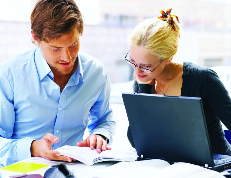 Two office workers using a laptop and book 