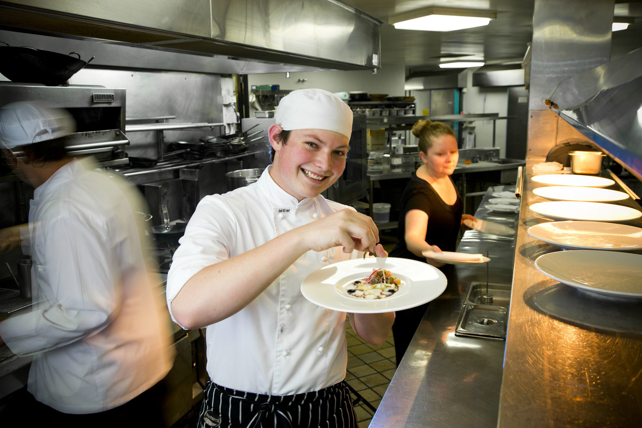 Young apprentice garnishing a dish in the kitchen