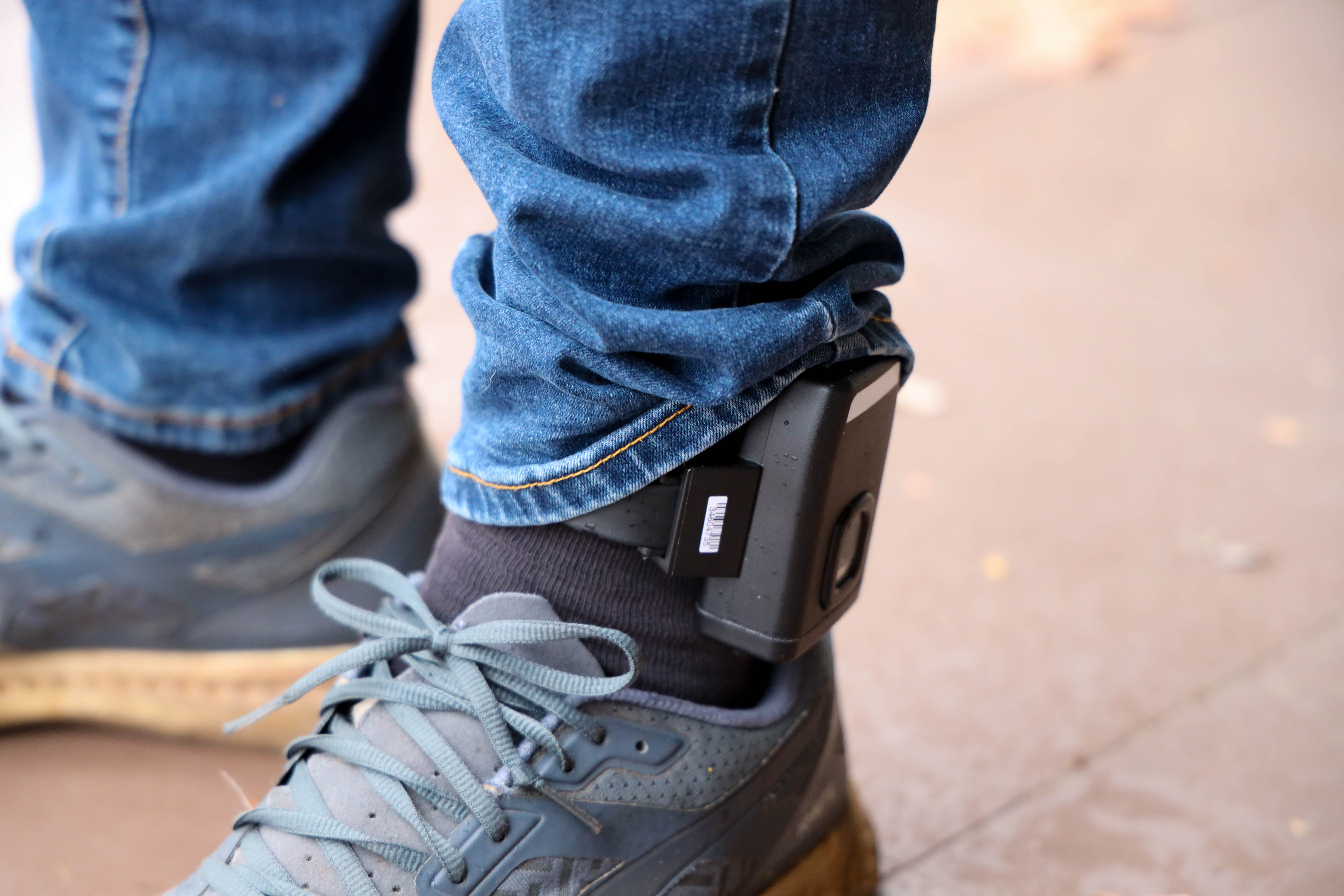 a man stands with an electric monitoring device on his ankle.