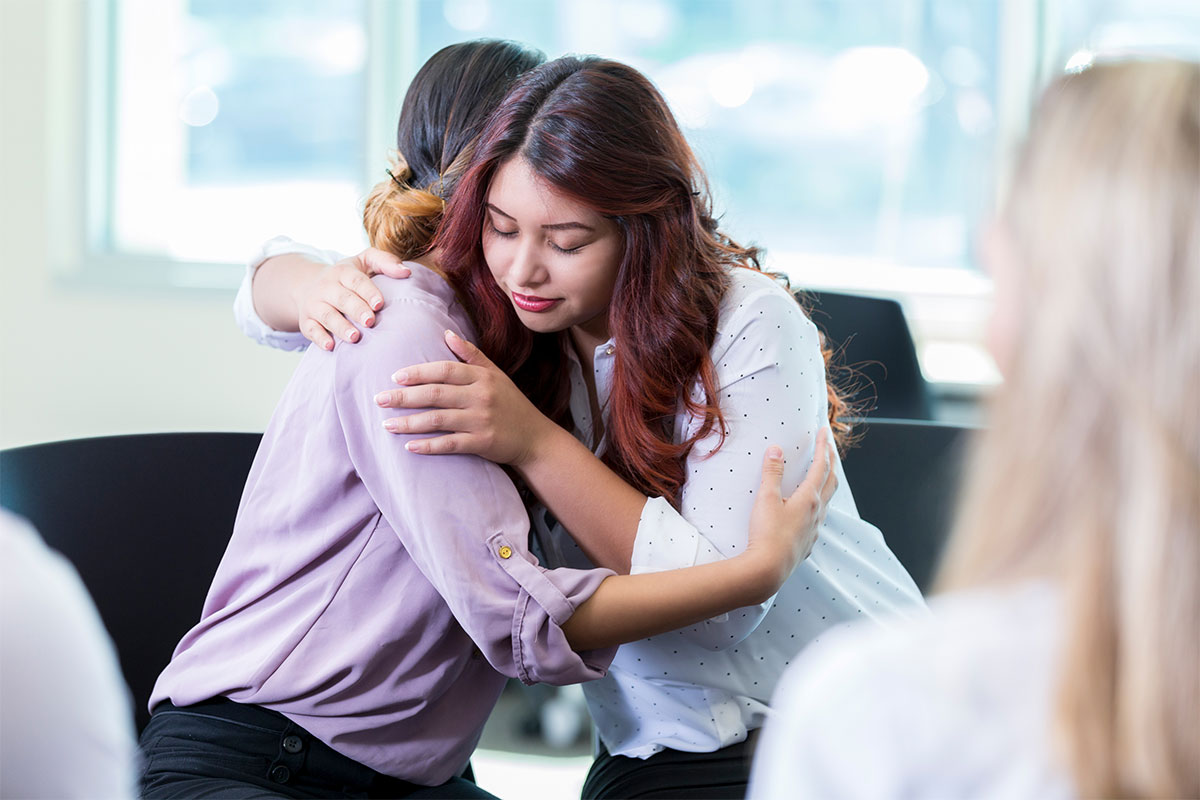 Two women seated hugging.