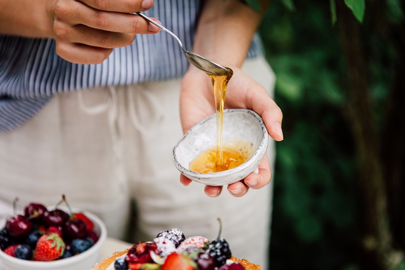 Man holding spoon with honey dripping into a small bowl