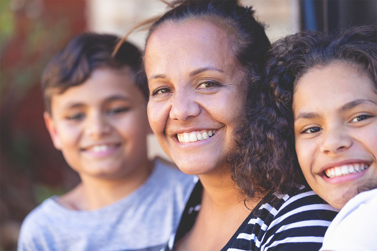 An Aboriginal mother with two young children, smiling.