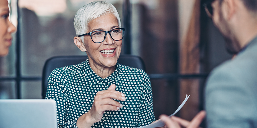 Image of a smiling middle age woman in an office with work colleagues 