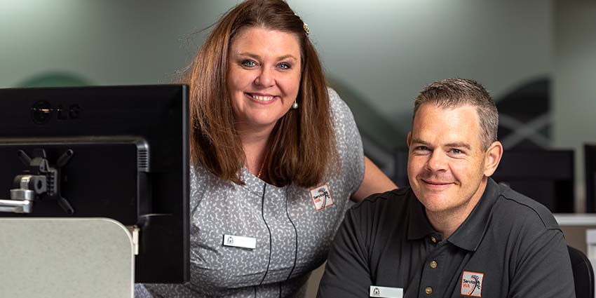 Two staff from the trial ServiceWA Bunbury centre smiling behind a desk