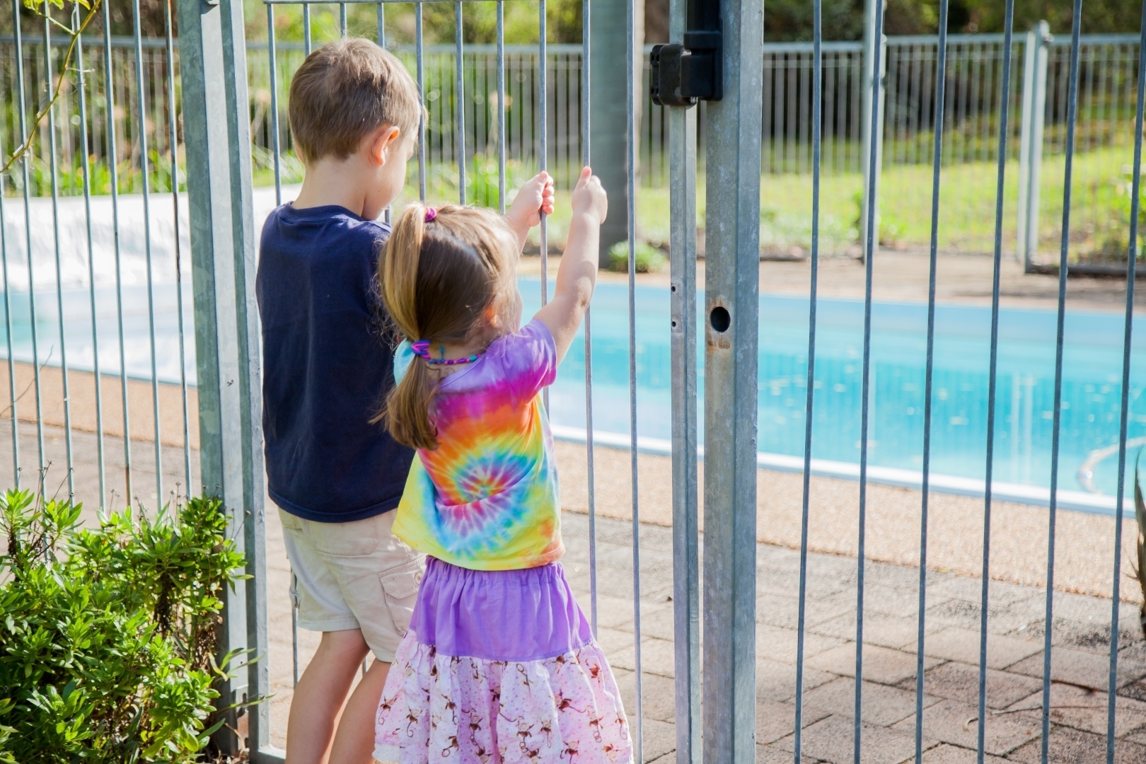 Two young children standing outside of a pool safety barrier.