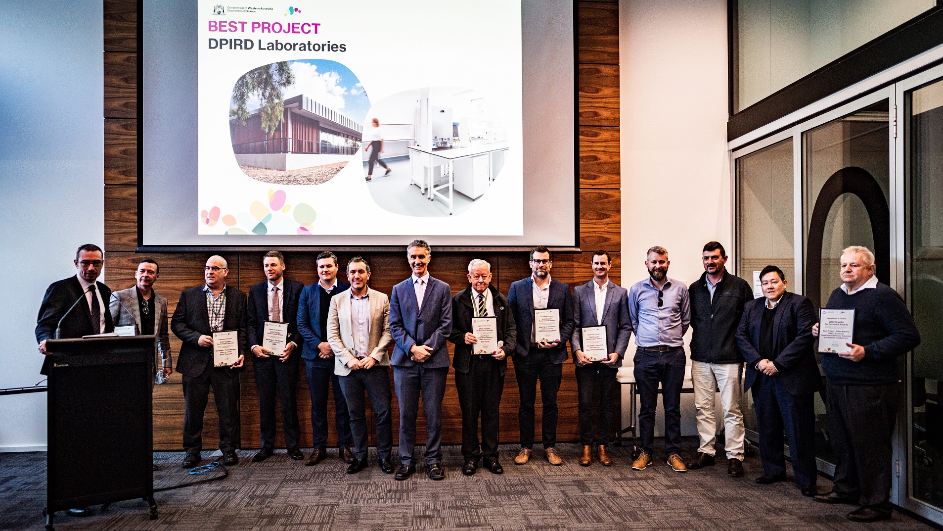 A line of people standing at the front of the room holding their certificates