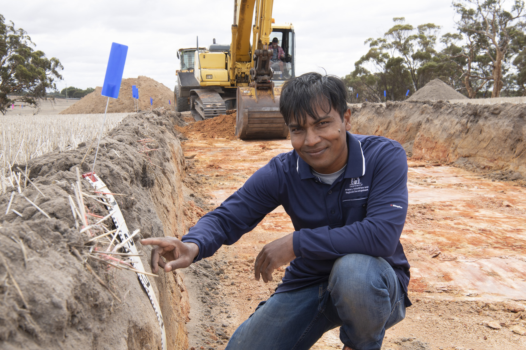 Dr Gaus Azam in a trial plot at Meckering, excavator and scraper vehicles in background.