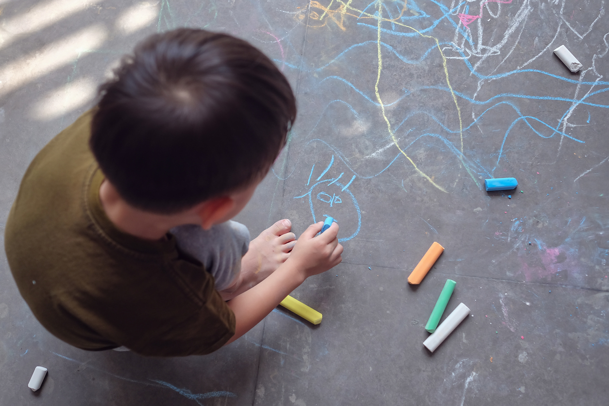 image of a young child playing with drawing with coloured chalk sticks