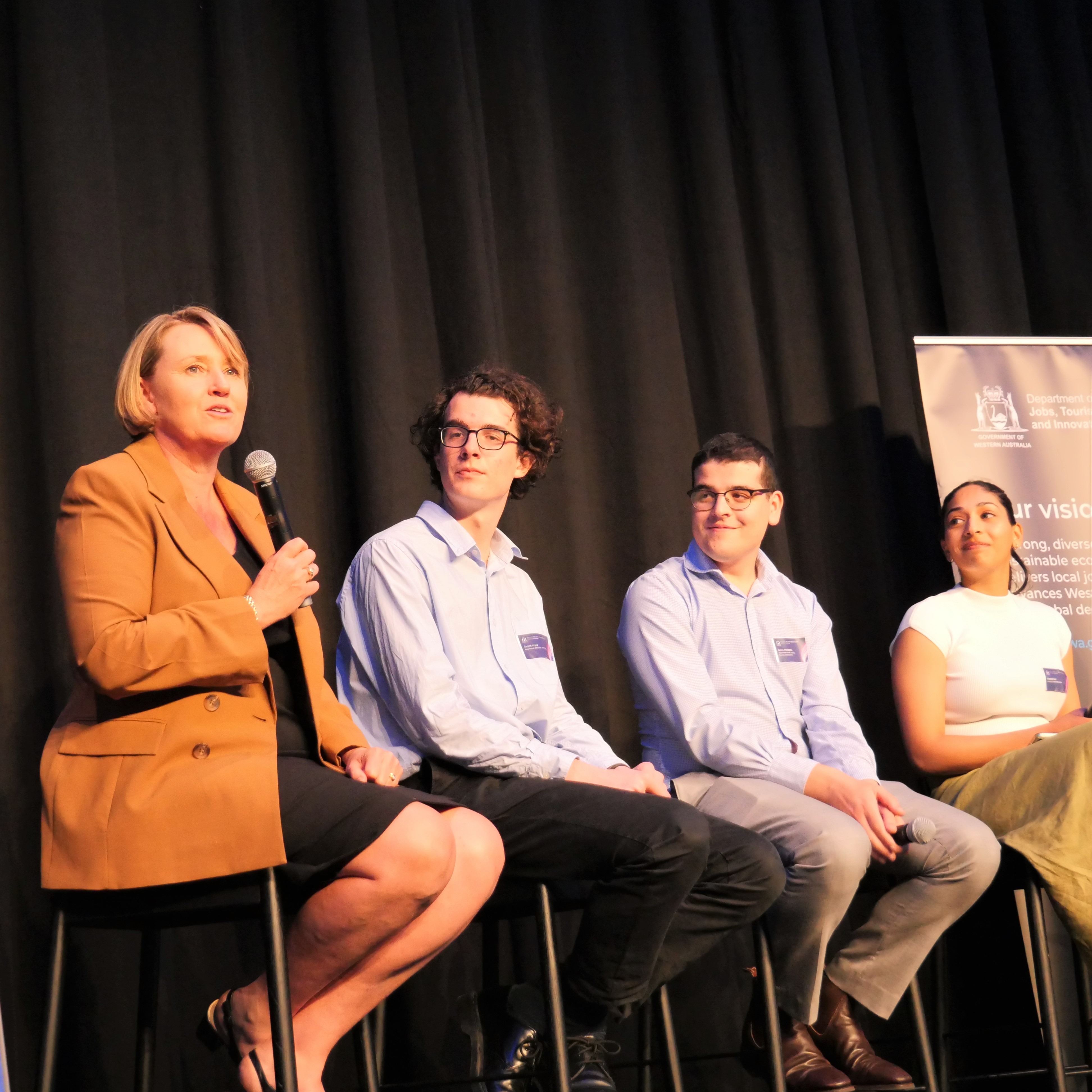 Group photo of the panel discussion at the Innovative future leaders event. Director General Rebecca Brown is holding the microphone and talking to the crowd. Beside her are three representatives from the crowd. 