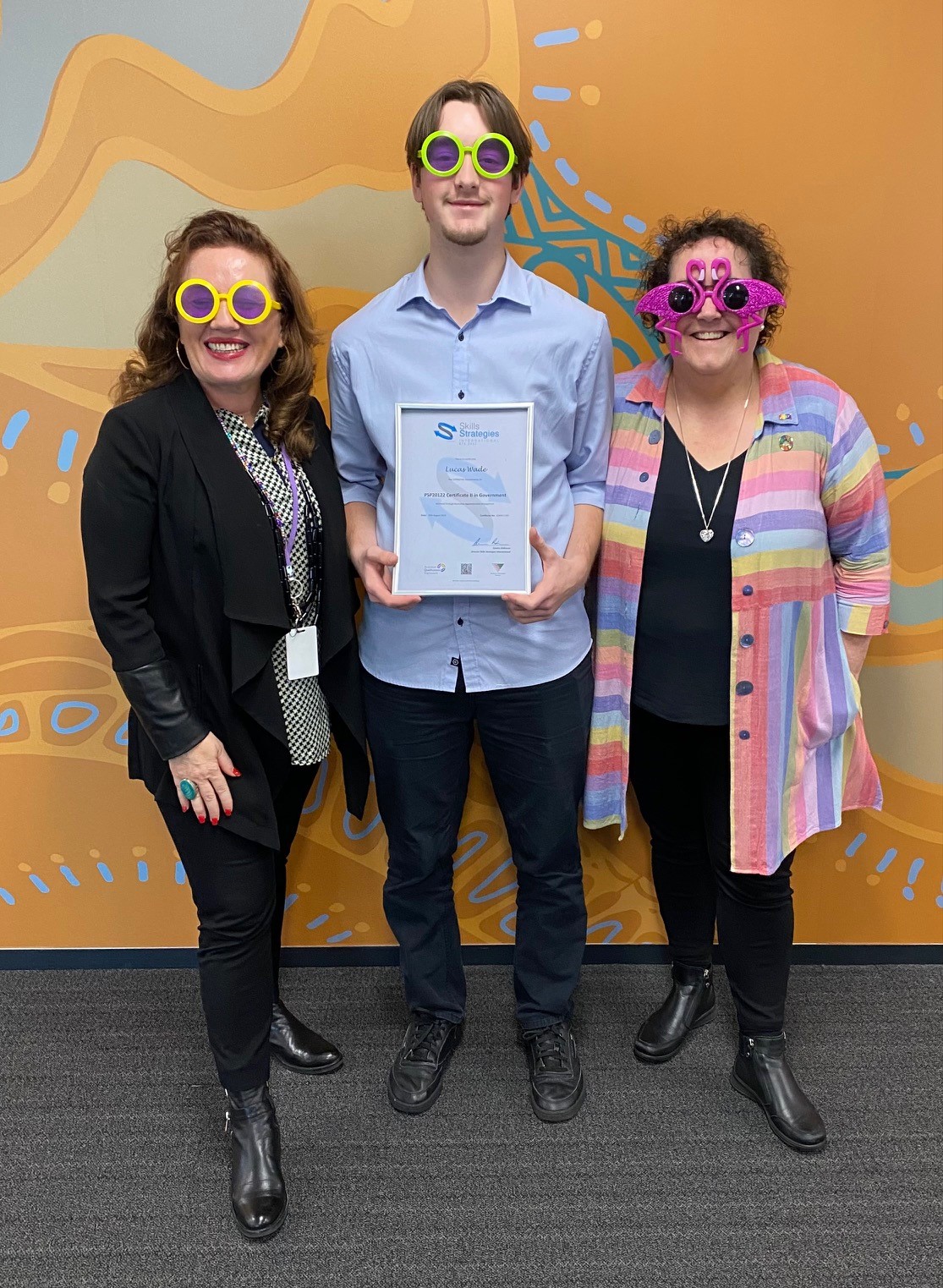 Photo of student Lucas Wade flanked by Communities staff and wearing funny sunglasses