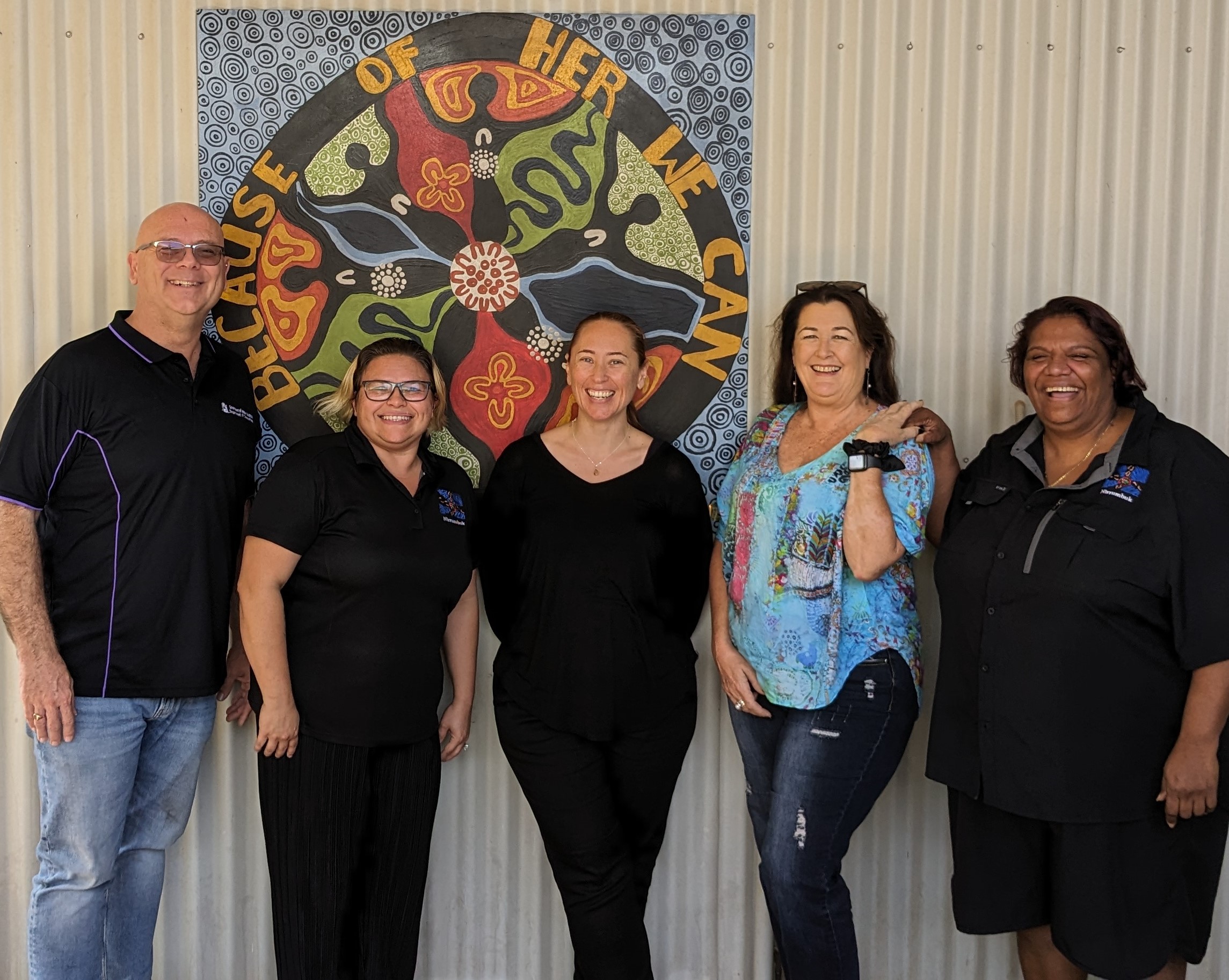 Five people standing in front of a wall and a bright painting.