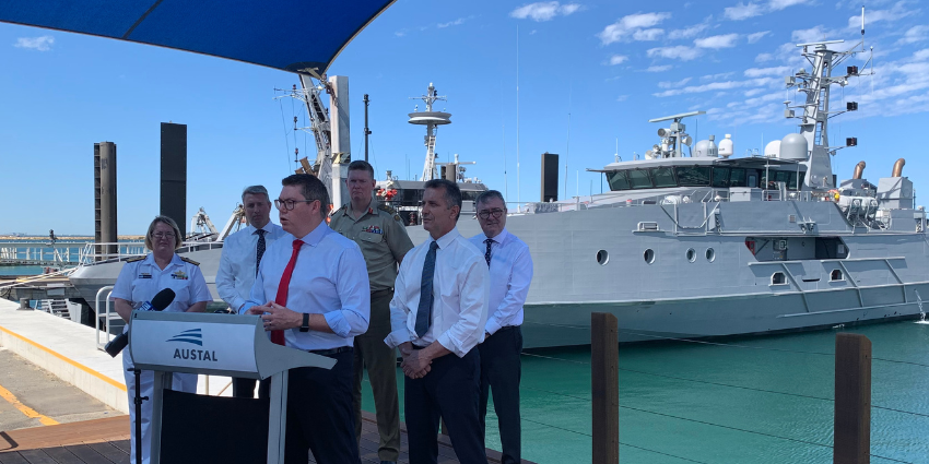 Representatives are standing behind the Austal Lectern. A vessel is in the background