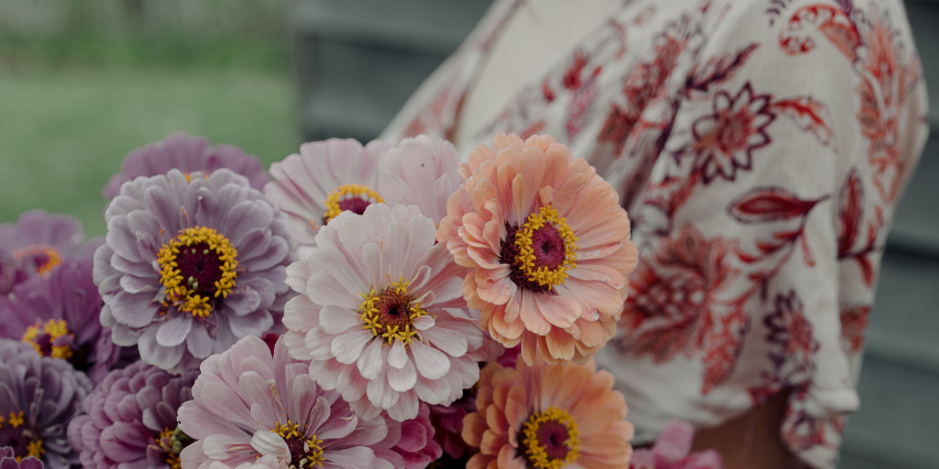 A woman in a pink floral dress is holding a bouquet of purple, pink and orange flowers