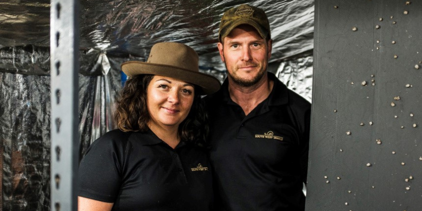 A man and a woman wearing black shirts are standing next to a wall of snails 