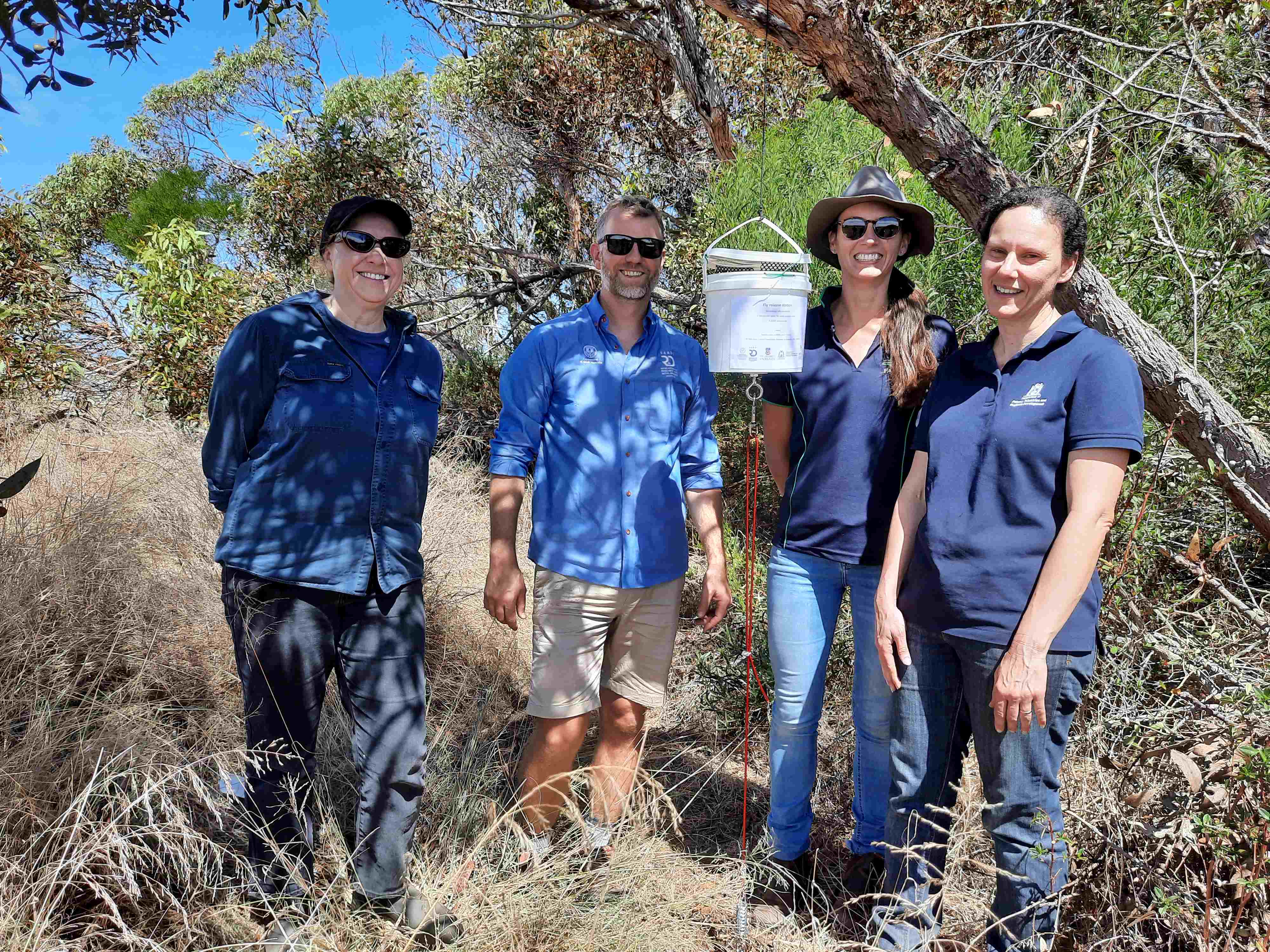 Three women and a man standing with a bucket hanging from a tree.