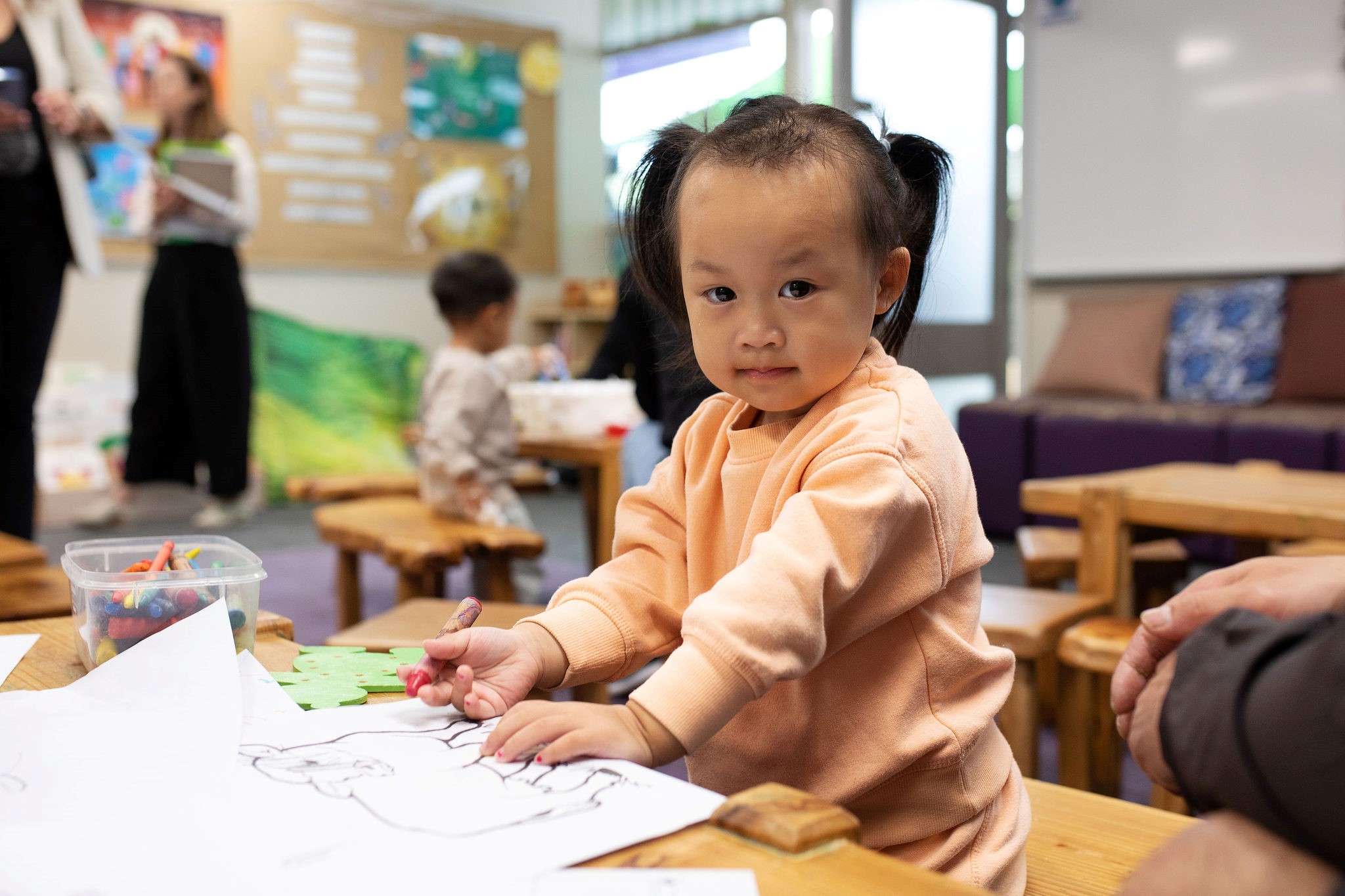 A young child sitting at a table, drawing with coloured crayons.