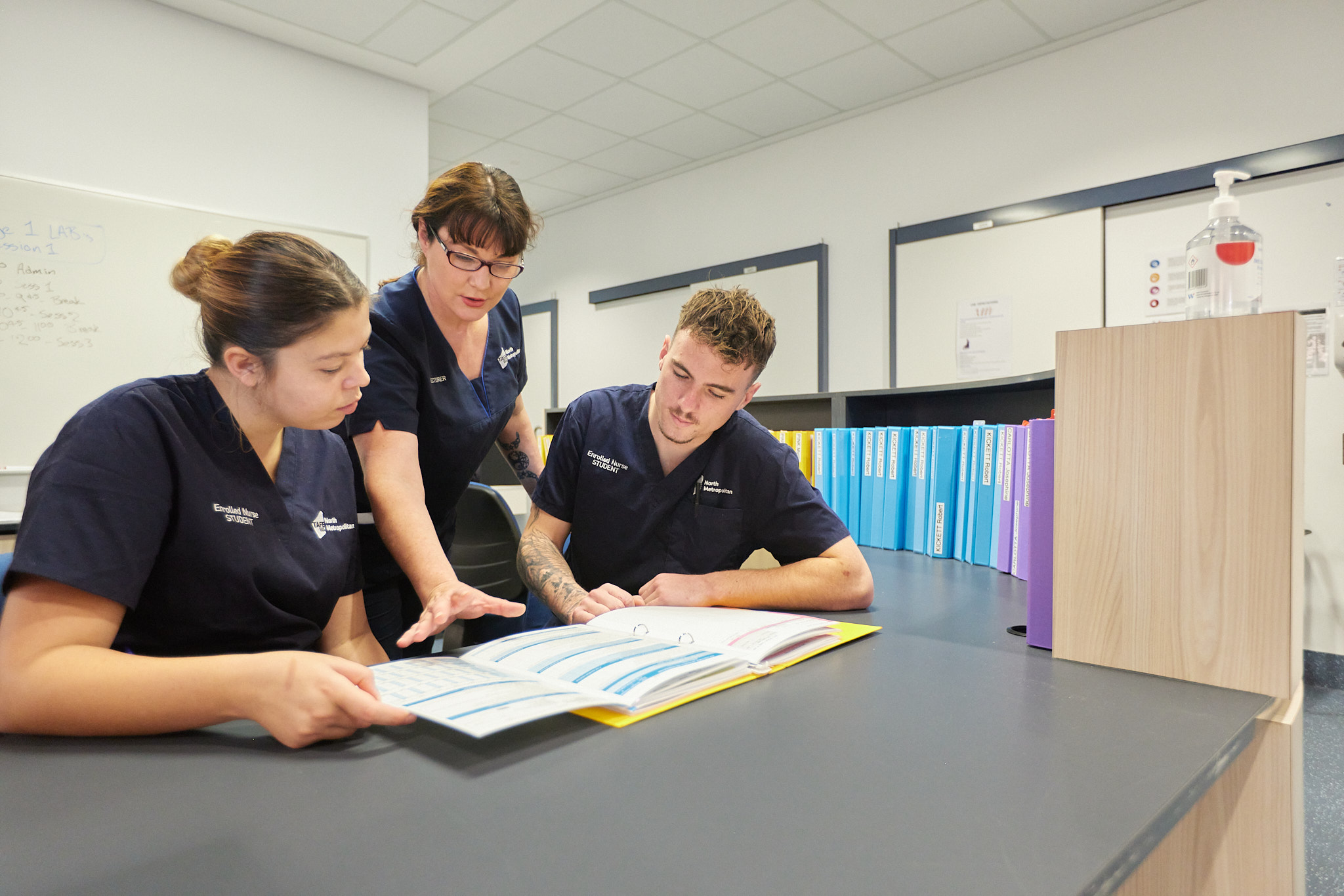 A nursing instructor guides two students through a study session, reviewing materials together at a table. 