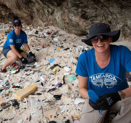 Two smiling volunteers crouching toward the beach sand collecting washed up litter.