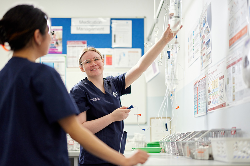 Two nursing students in navy scrubs, working in a clinical setting. 