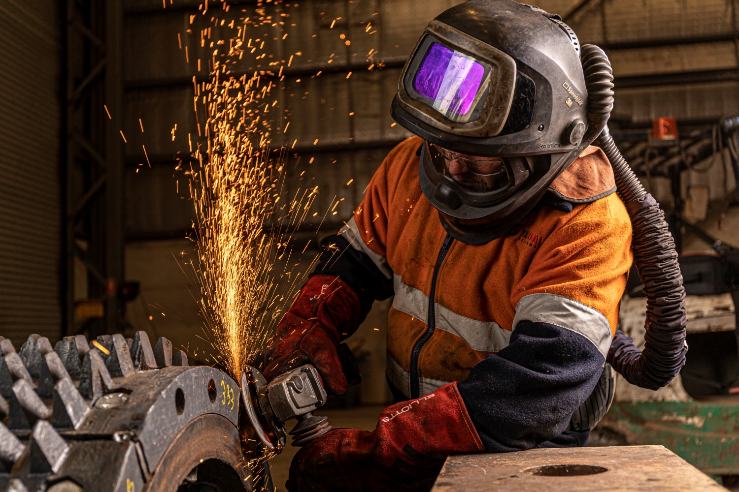 worker in safety gear with machine and sparks flying