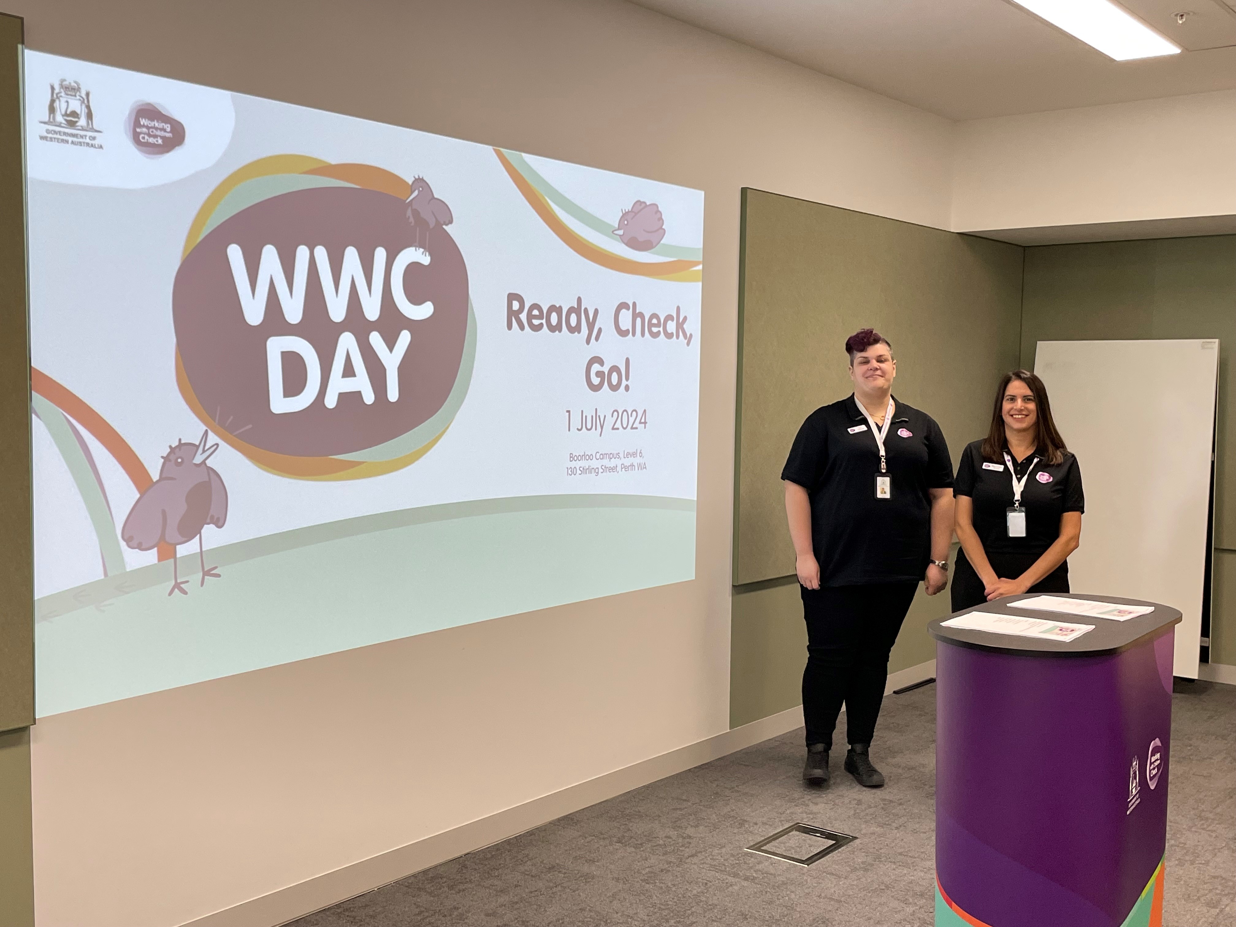 Photo of two Working with Children staff in an office environment with a Working with Children Day banner in the background