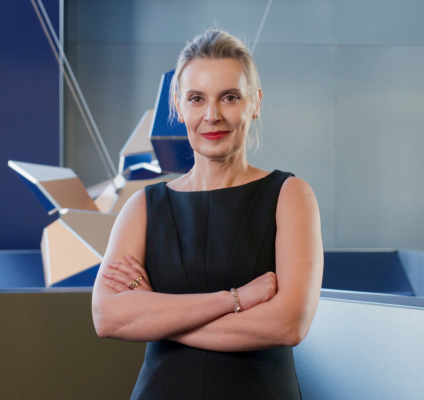 A woman in a black dress poses elegantly in front of a vibrant blue wall