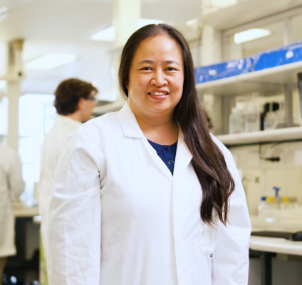 A woman in a lab coat stands confidently in front of a laboratory