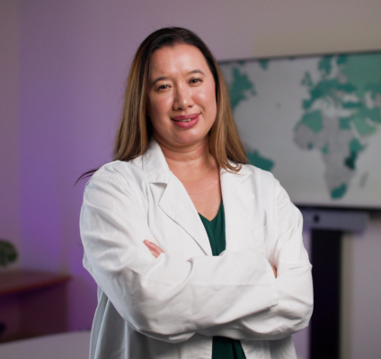 A woman in a lab coat stands confidently in front of a television,