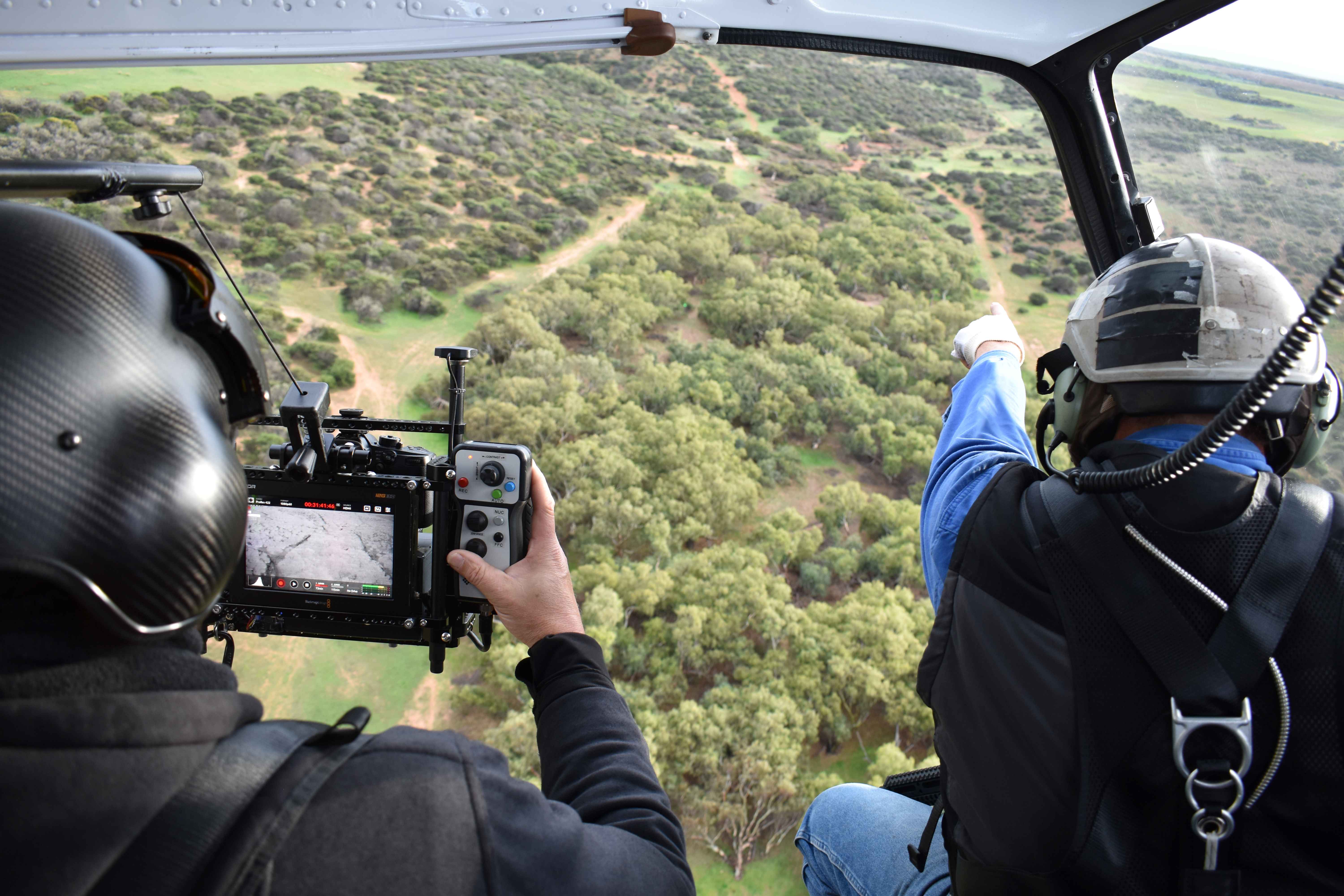 An aerial view of two people in a helicopter scanning the landscape.