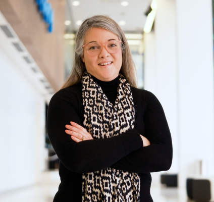 In a bright hallway, a woman dressed in a black shirt and scarf stands, showcasing her stylish and composed demeanor.