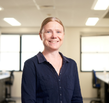 A woman wearing a blue shirt stands confidently in a modern office environment, surrounded by professional decor.