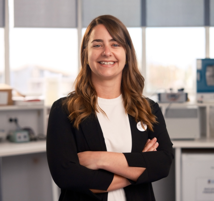 A woman in a black blazer is positioned in front of a desk, representing a professional in a laboratory environment.