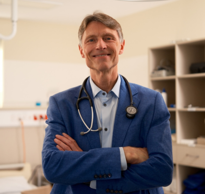 A man in a blue suit stands confidently in a hospital room, surrounded by medical equipment