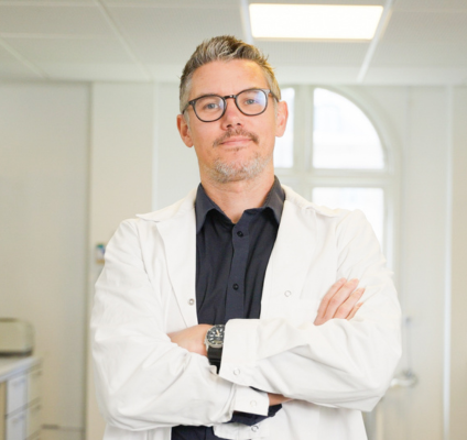 A man in a lab coat stands confidently in front of a desk, showcasing a professional laboratory environment.