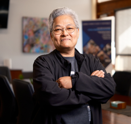 a woman with short grey hair  An older woman wearing glasses stands confidently in front of a desk