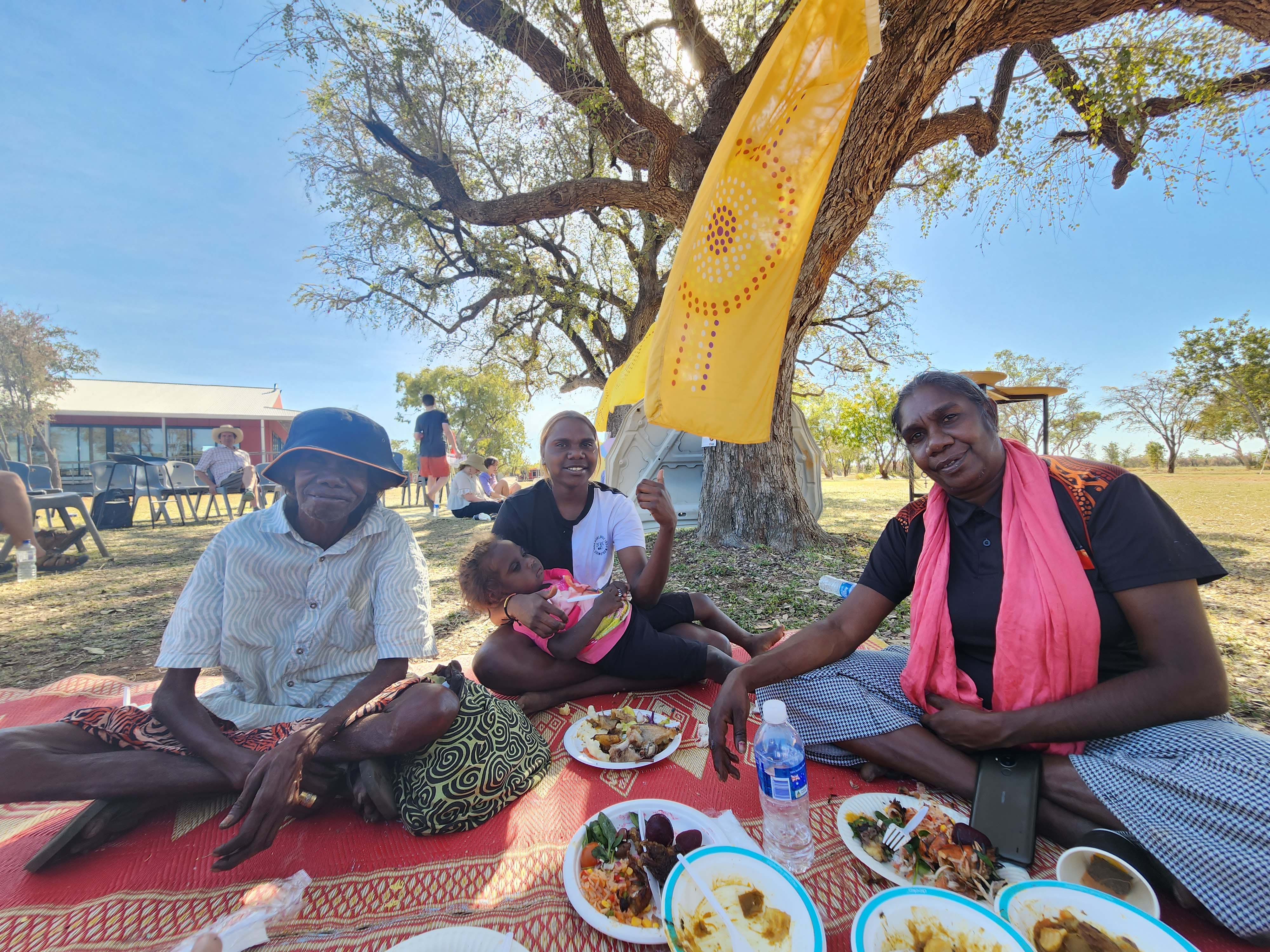 A group of 4 individuals sitting on a picnic blanket with plates of food in front of them.