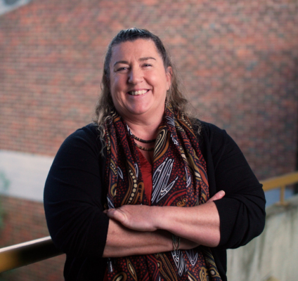 A woman stands on a balcony with her arms crossed