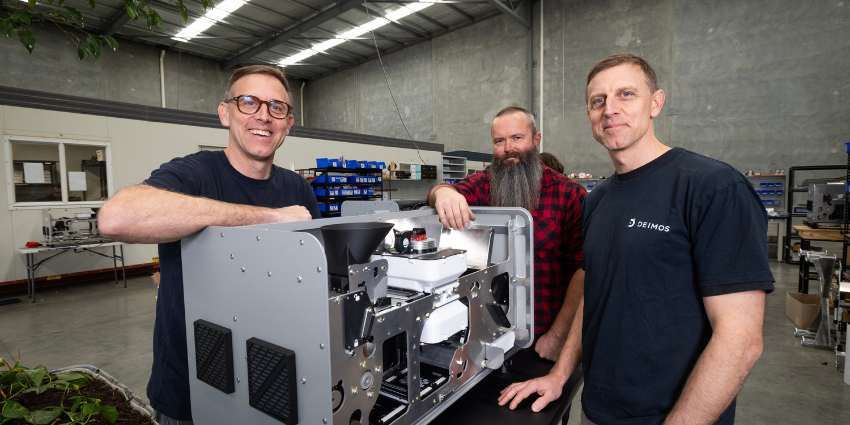 three men standing around a metal machine for grain similar to a coffee machine