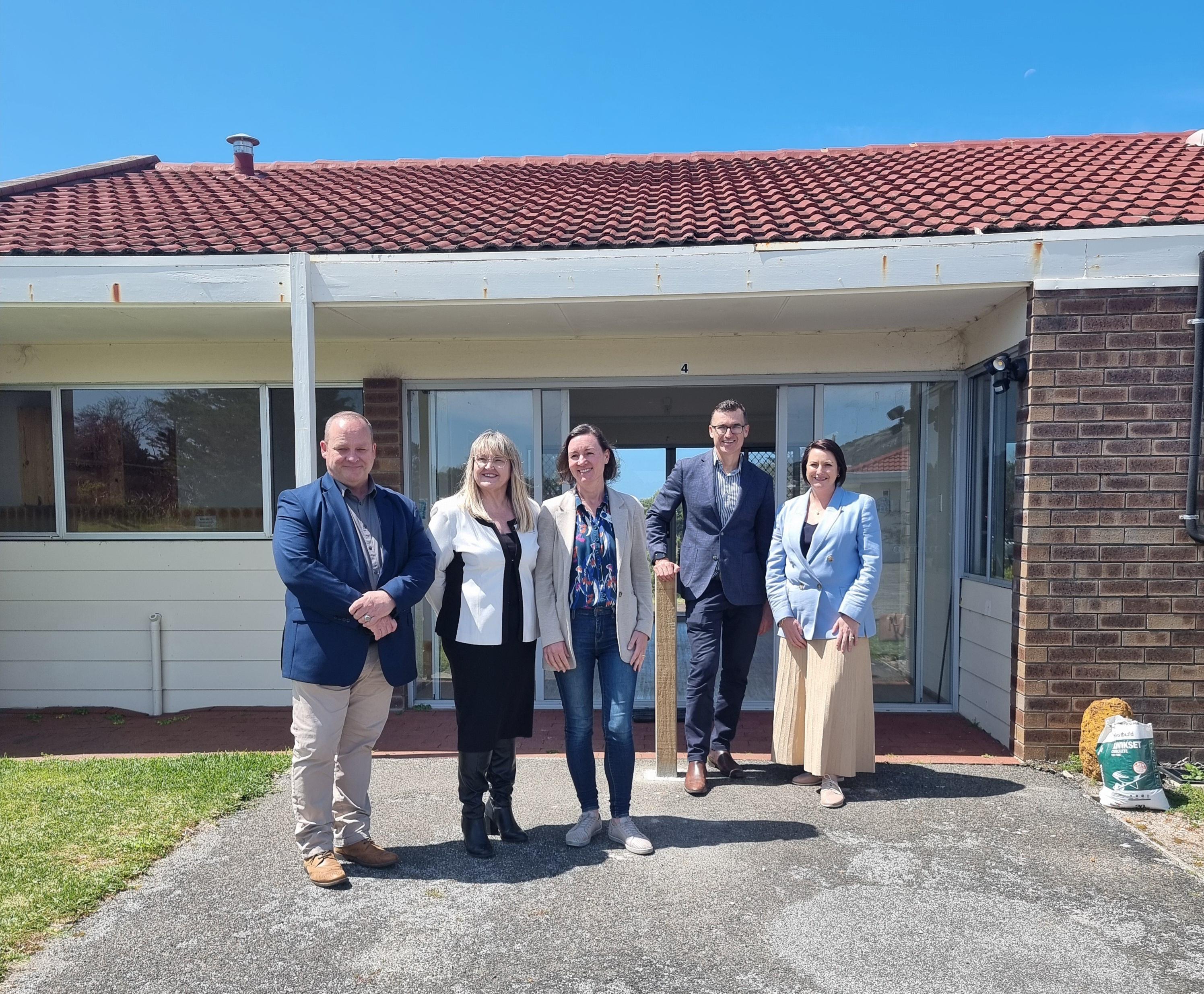 group photo of Minister Carey and four stakeholders (three women and a man) in front of a house