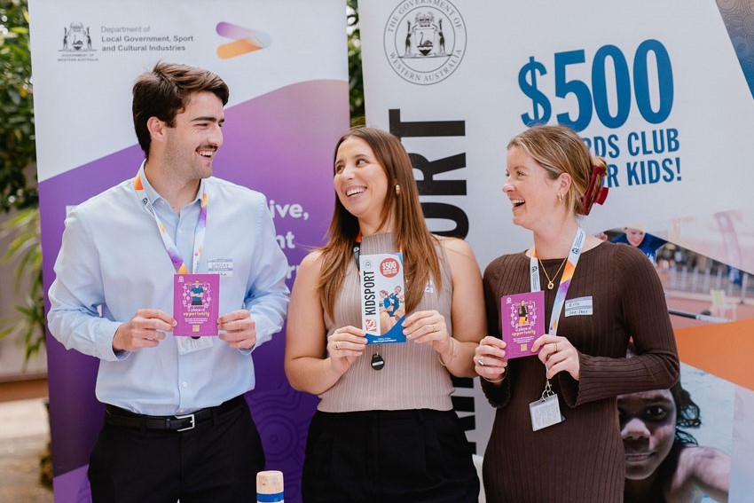 Three young employees smiling and holding graduate program flyers