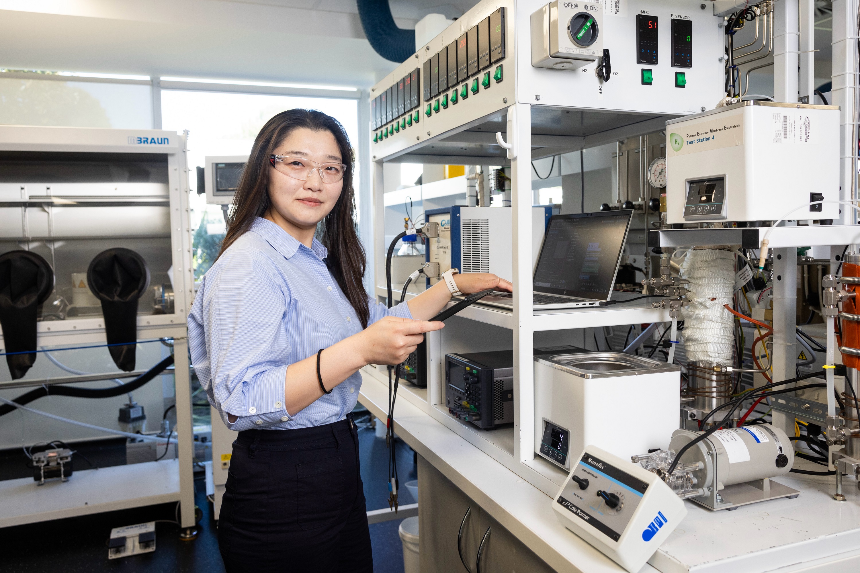 young asian girl working in a scientific lab, wearing blue dress shirt and black trousers and safety glasses