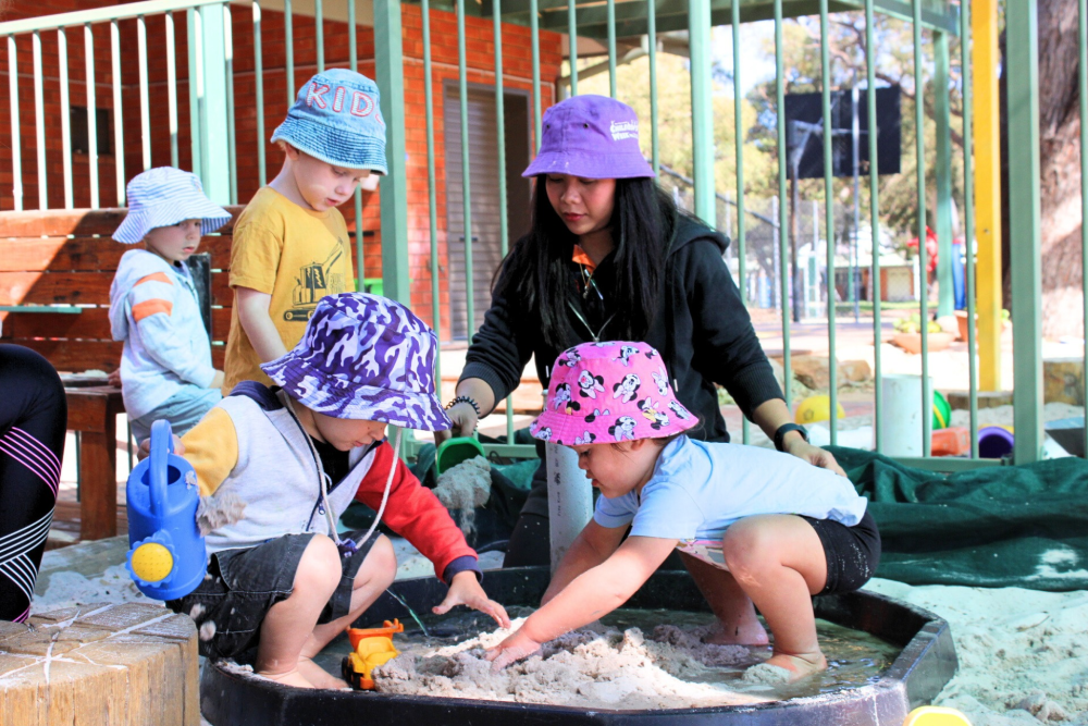 Photo of a early childhood education and care playground with children and a female educator playing together