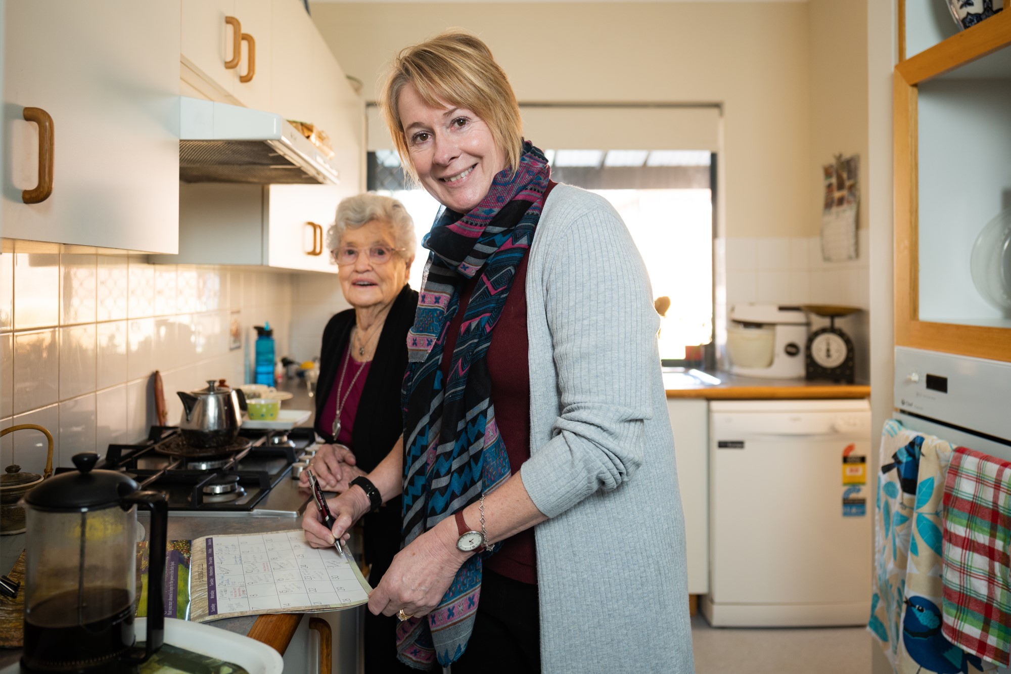 photo of a woman assisting an elderly woman in the kitchen of a house