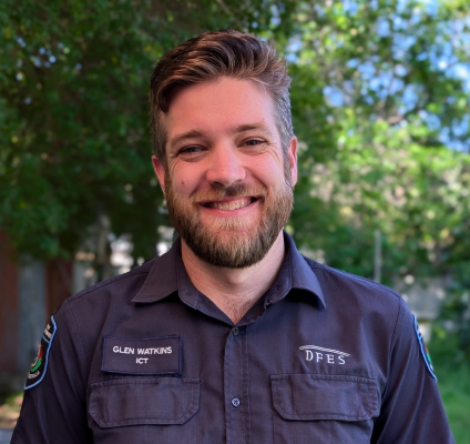 man in blue polo standing in front of greenery and smiling