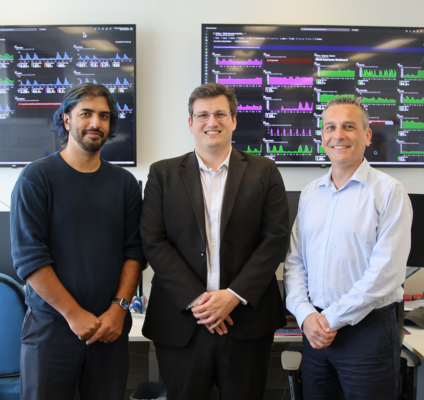 three men standing in office with charts behind them