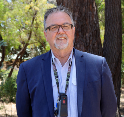 Man in a shirt with lanyard and blue blazer smiling at camera