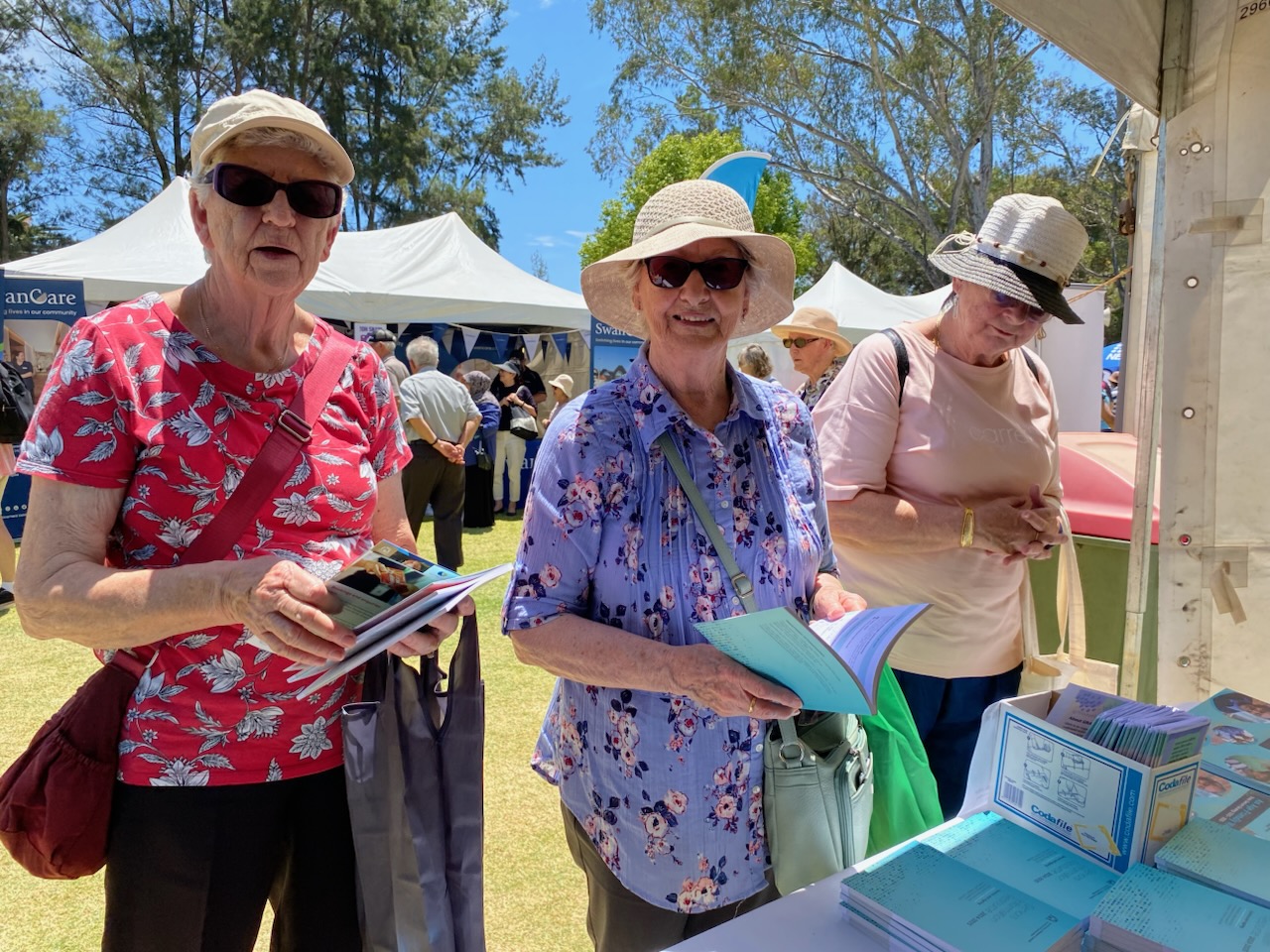 Photo of three women in a park reading copies of the Seniors Information Resource booklet