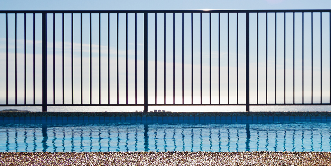 This image depicts a panel of swimming pool fencing with a pool in the foreground.